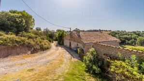 Una casa de piedra con techo de tejas, un camino de grava y follaje circundante.