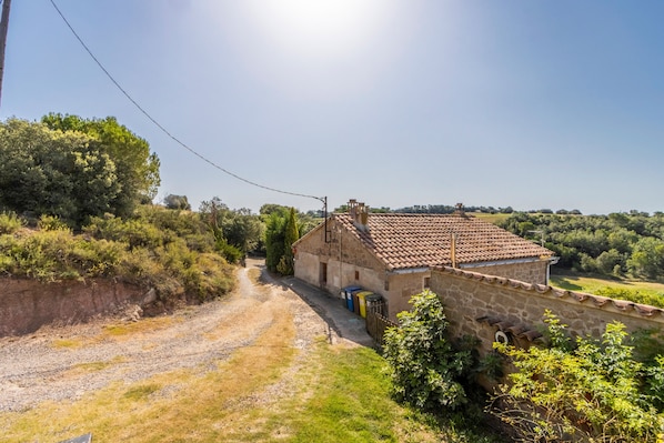 A stone house with a tiled roof, a gravel path, and surrounding greenery.