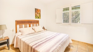 Un dormitorio con cabecera de madera, cama con manta a rayas, mesita de noche con lámpara y ventana con persianas.