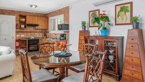 Una cocina moderna con armarios de madera, un microondas y un comedor con mesa y sillas de vidrio.