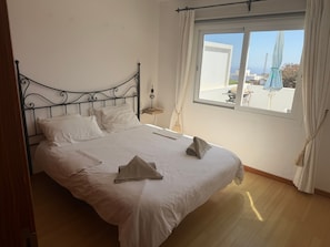 Un lit bien fait, avec des oreillers et une serviette pliée, une table de chevet avec une lampe et une fenêtre avec des rideaux.
