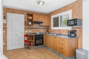 Une cuisine avec des meubles de rangement en bois, un four encastré, un four à micro-ondes et une fenêtre avec des stores.