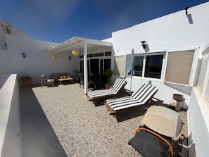 Un espace extérieur aménagé, abrité et doté de fauteuils confortables et d’une table, ainsi que d’une plante en pot et d’un barbecue.