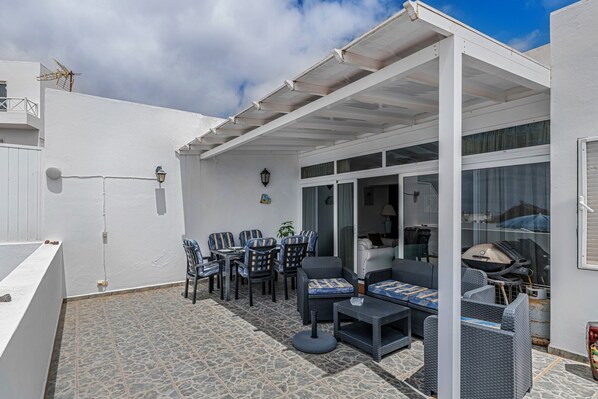 Un patio exterior techado con zona de estar, una parrilla y vistas al interior.