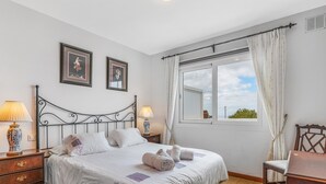 Una cama bien hecha con sábanas blancas, dos lámparas de noche y una ventana con cortinas.