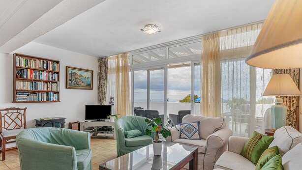 Una sala de estar con sofá, sillas, una mesa de centro, una estantería, televisor y un ventanal grande.