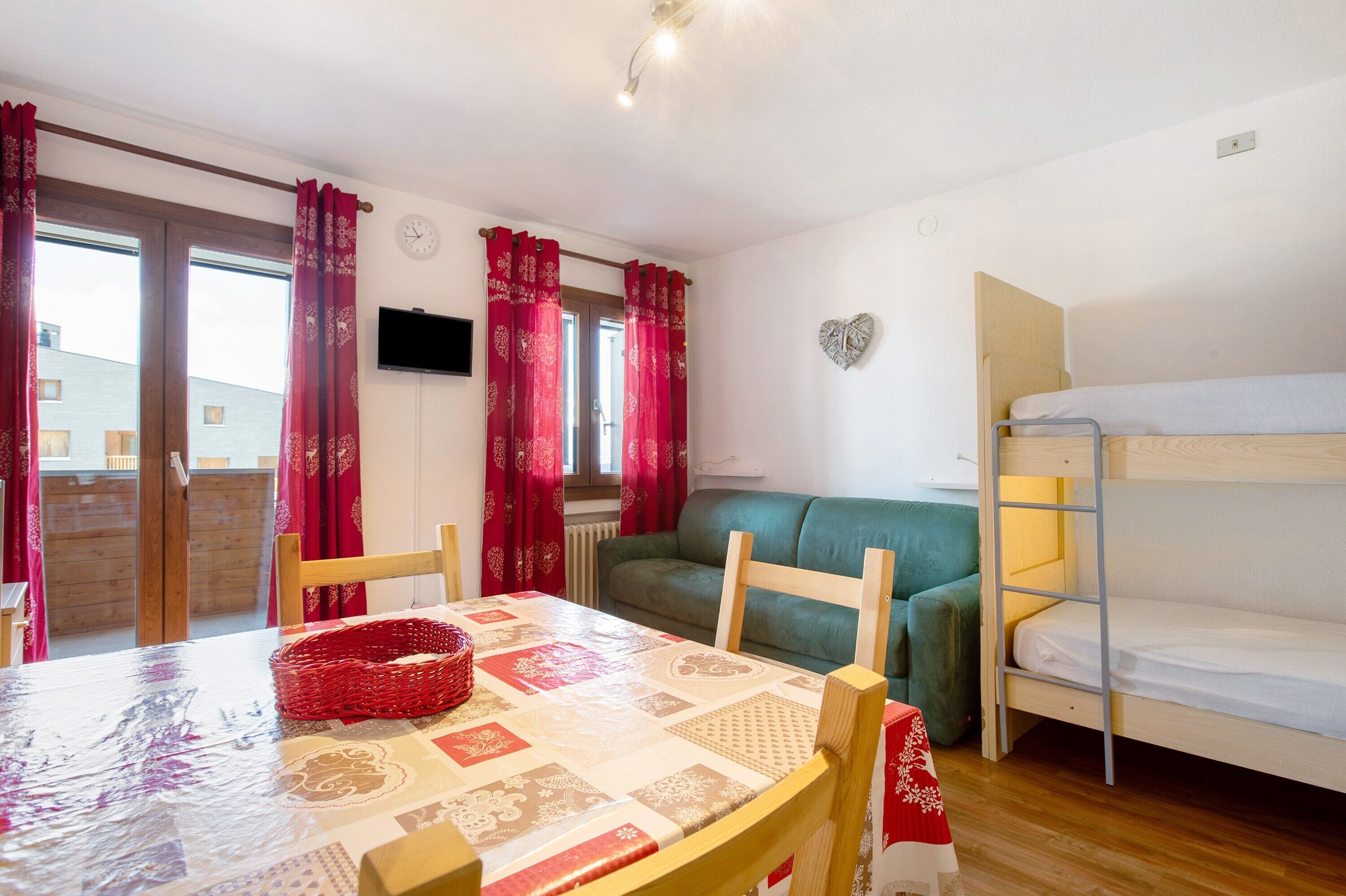 A room with a bunk bed, a sofa, a dining table with chairs, and a window with curtains.