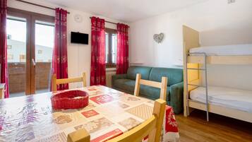 A room with a bunk bed, a sofa, a dining table with chairs, and a window with curtains.