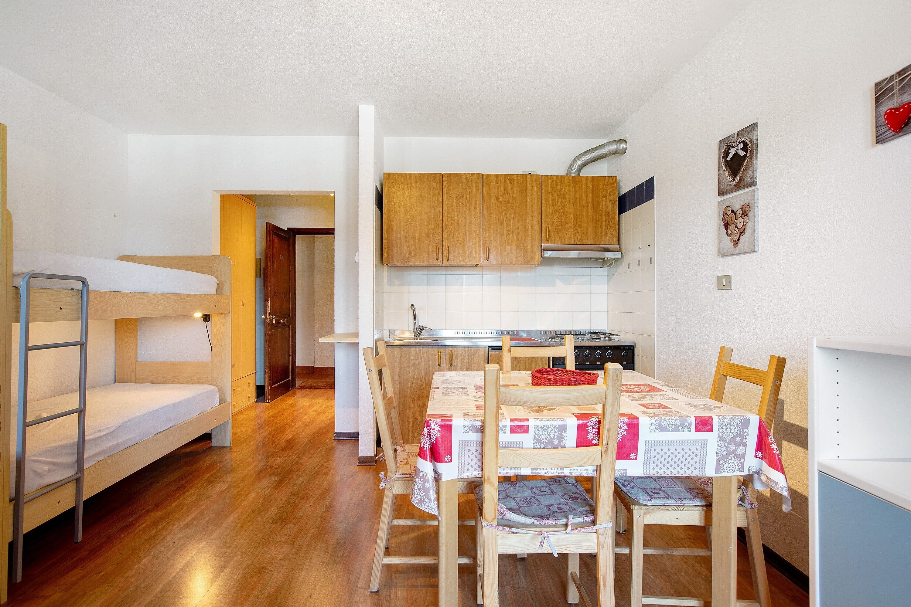 Une pièce de taille modeste comprenant un lit superposé, une table à manger avec des chaises, un coin cuisine et des placards en bois.