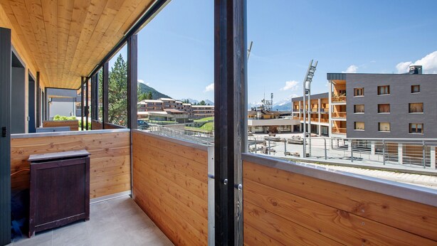 Un balcon avec des balustrades en bois, une vue sur des immeubles et un ciel dégagé.