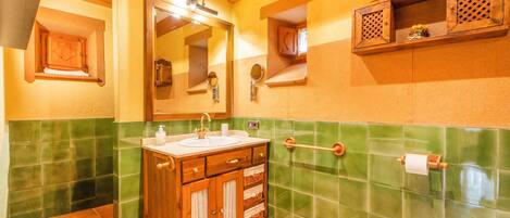 A bathroom with a wooden vanity, green tiled walls, a mirror, and a towel rack.