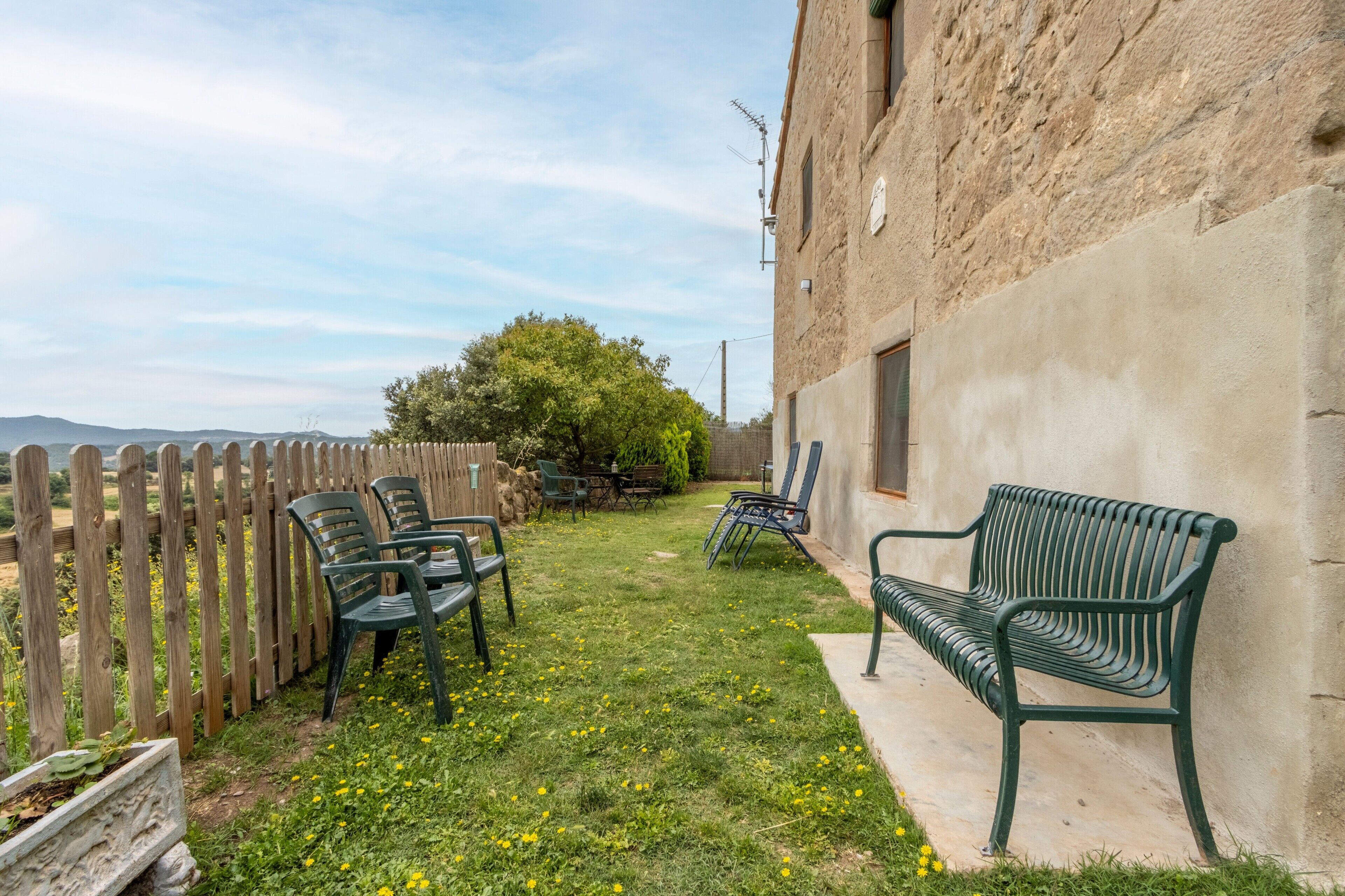A patio with a wooden fence, a green bench, and outdoor furniture.