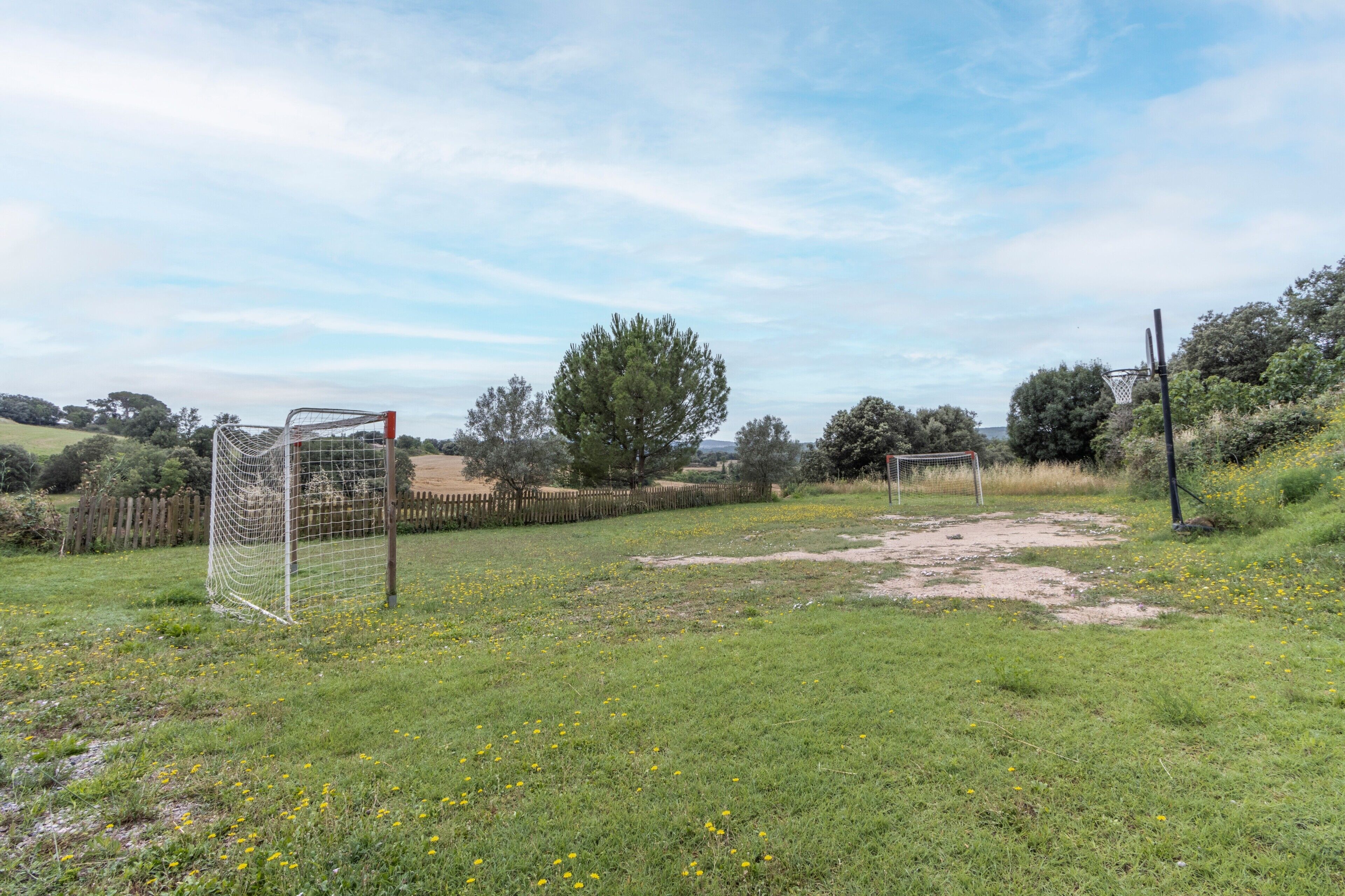 Un champ herbeux avec des buts de football, des arbres et une clôture.
