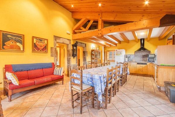 Un comedor con una mesa larga, sillas de madera, un sofá rojo y una cocina con armarios de madera y electrodomésticos.