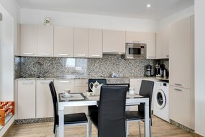 A modern kitchen with a dining area, granite countertop backsplash, stainless steel appliances, and a built-in washer and dryer. - Vacation Home 'Garten Apartment' with Sea View, Private Terrace and Wi-Fi (Tías)