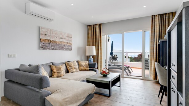 Una sala de estar moderna con un sofá, una mesa de centro y un televisor. Hay un balcón con vistas.