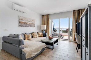 Uma sala moderna com sofá, mesa de centro e televisão. Possui uma varanda com vista.