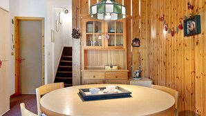 Une table ronde en bois, sur laquelle se trouve un plateau avec des tasses et des soucoupes, un meuble avec des portes en verre et un escalier.