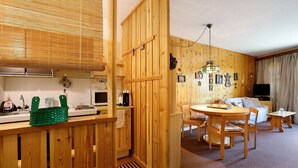 Un intérieur en bois comprenant une cuisine, un coin repas et un salon, avec un mur en bois, une table à manger avec des chaises, un canap é et un téléviseur.