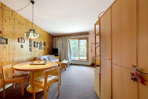 Una habitación con paredes de madera, una mesa redonda para comer, sillas, un sofá, un televisor y una ventana con cortinas.
