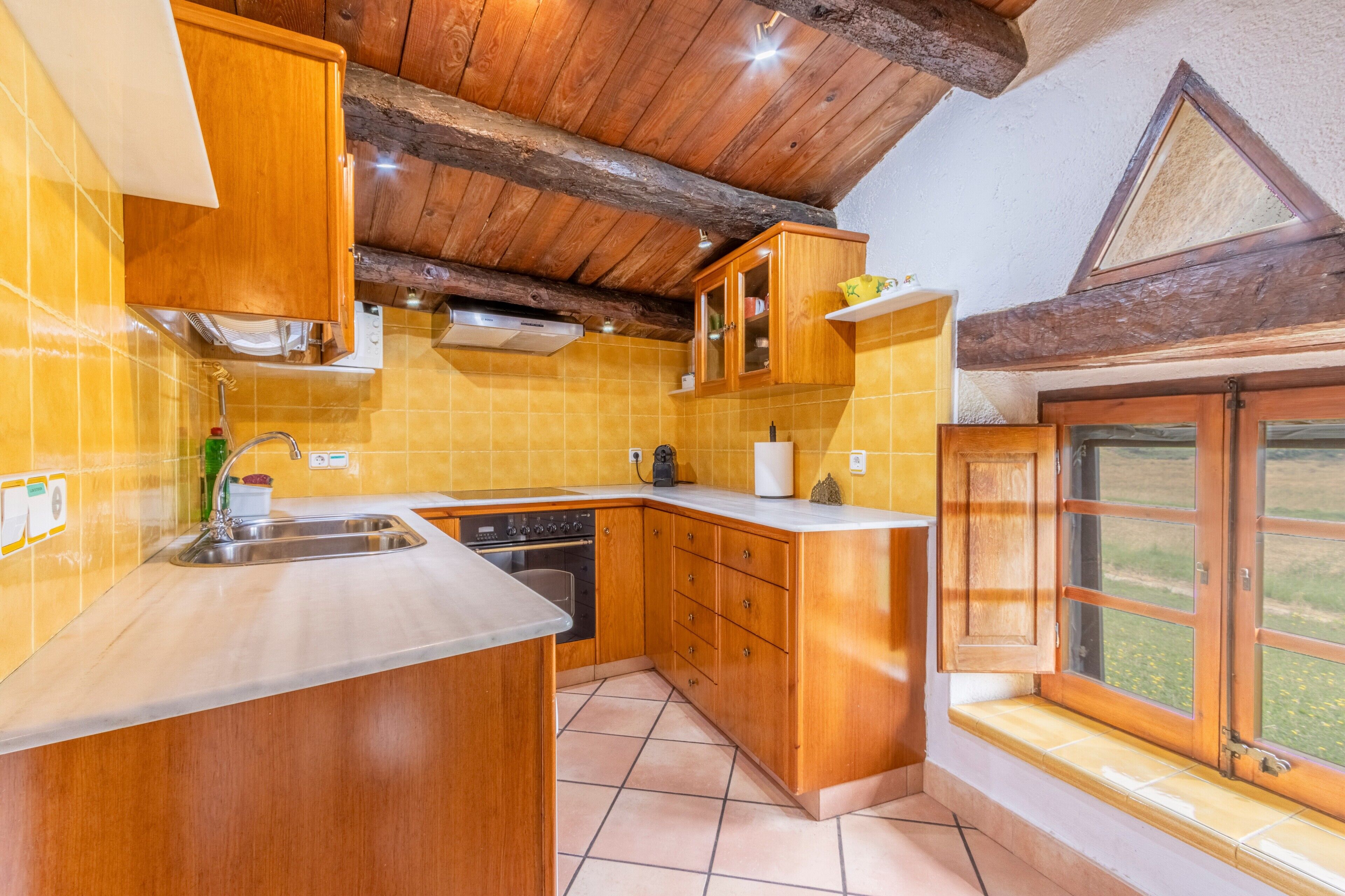 Een keuken met houten kastjes, een spoelbak en een raam met uitzicht.