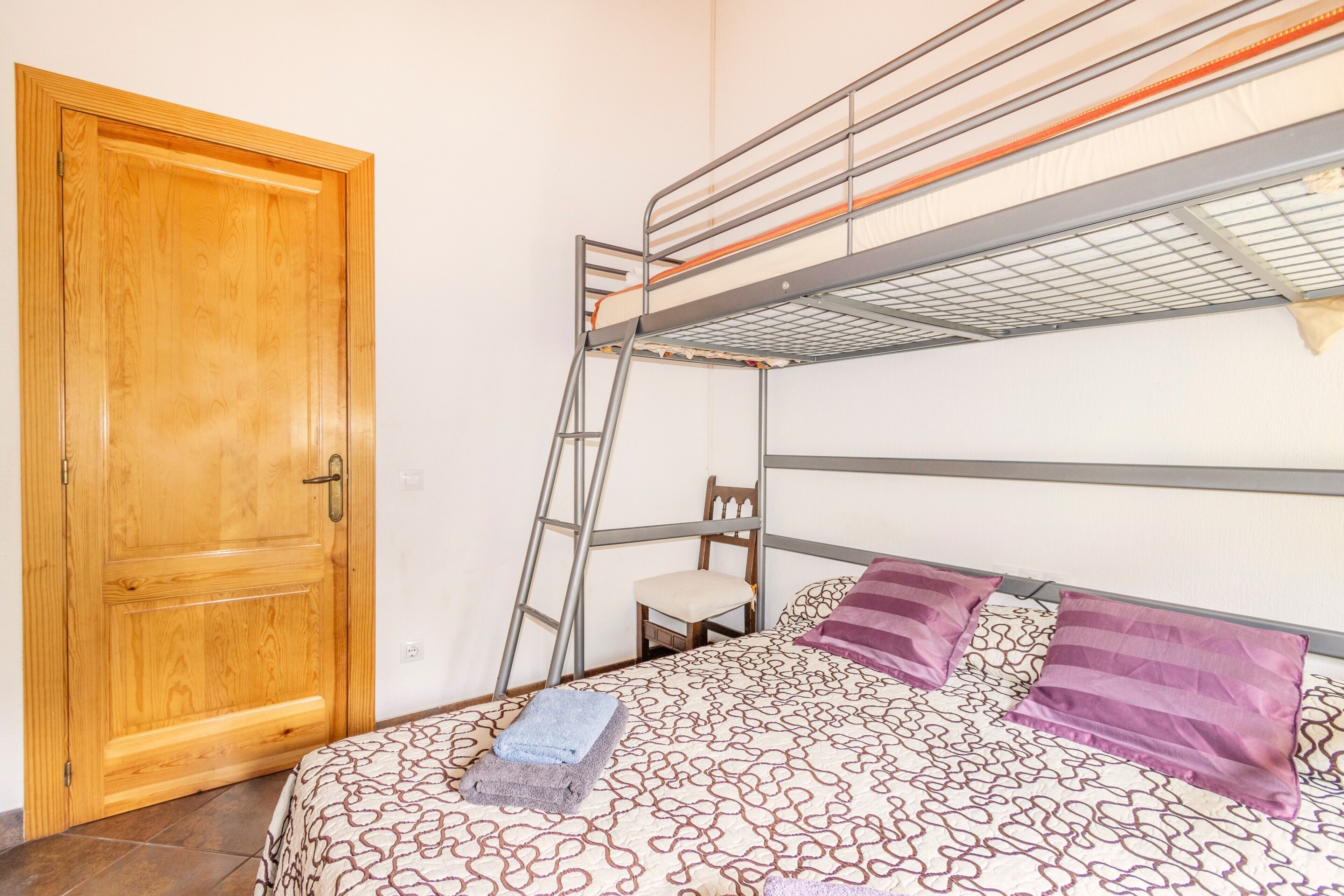 Una cama litera con escalera, una puerta de madera y una colcha estampada.