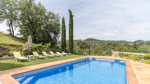 A swimming pool with a patterned edge, surrounded by a grassy area with lounge chairs and tall trees. - Holiday Home 'La Granja' with Mountain View, Wi-Fi and Air Conditioning (Olvan)