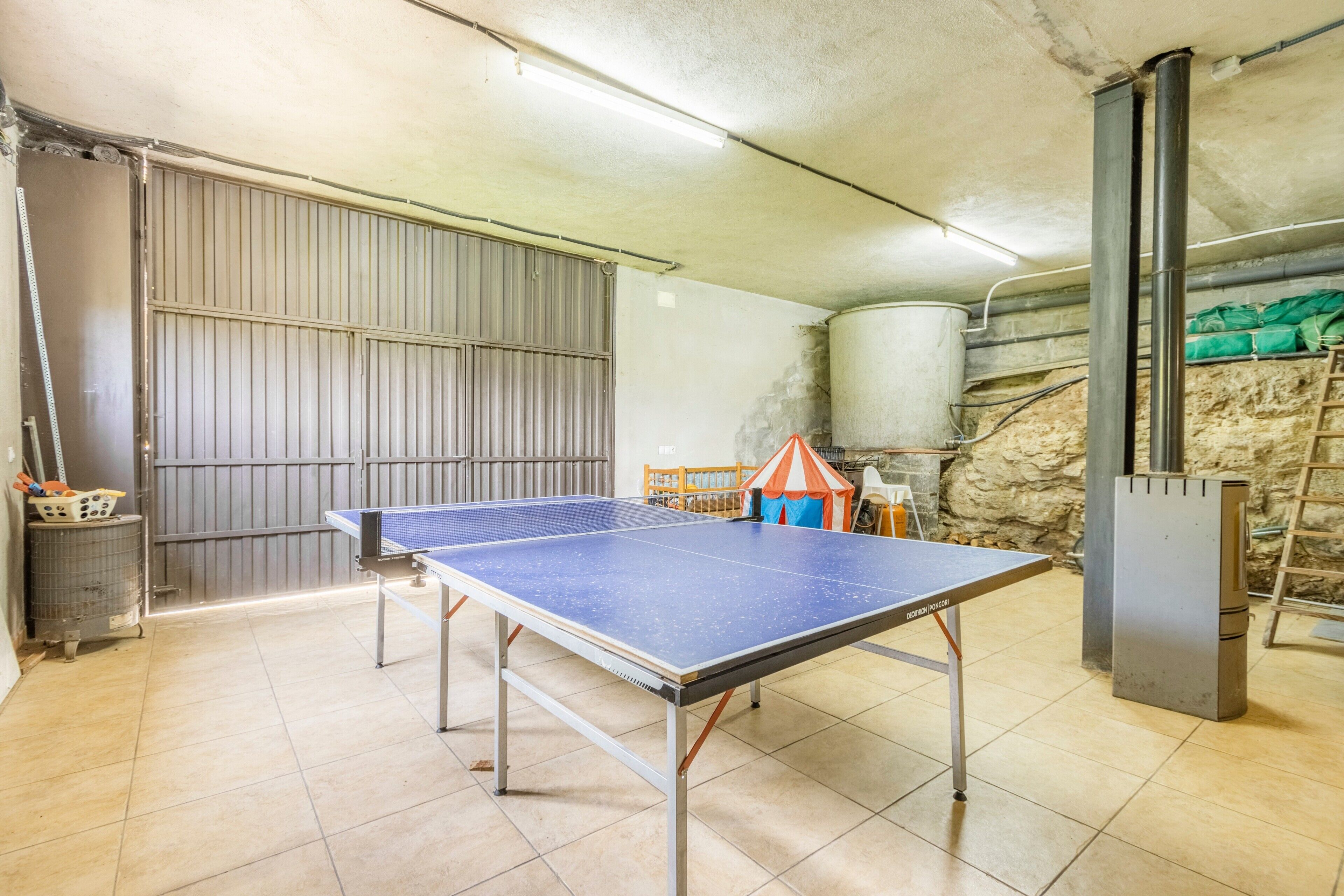 Taula de ping-pong en una habitació amb sòl de rajola, una porta metàl·lica i un dipòsit d'aigua.