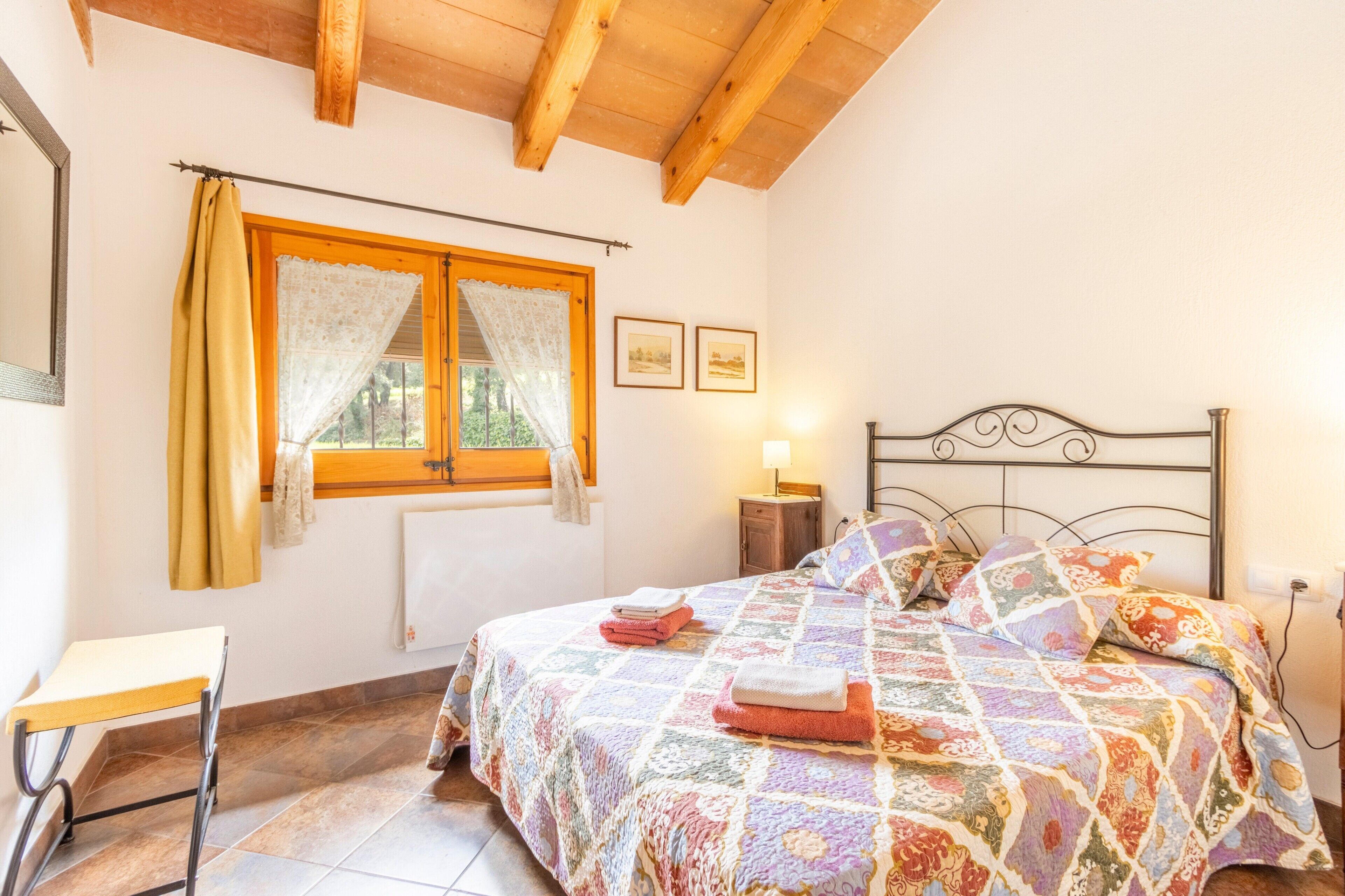 A bedroom with a bed, a window with curtains, a bedside table, and a nightstand.