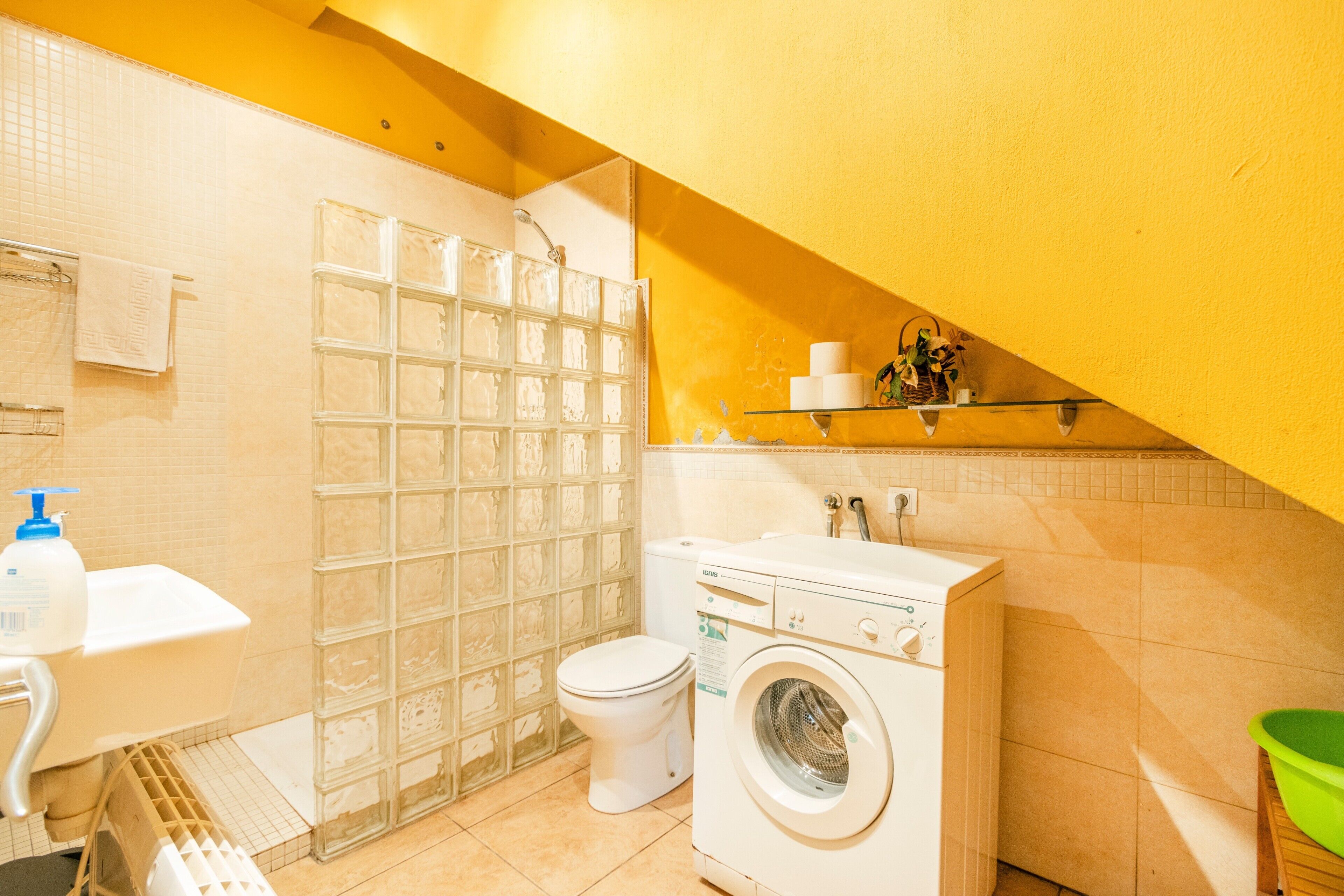 Un baño pequeño con ducha, inodoro, lavadora y estante con artículos de aseo.