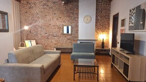 Un salon avec un mur en briques, un canapé, un fauteuil, une table basse, une cheminée et un téléviseur.