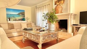 A living room with a beige sofa, a glass coffee table, a fireplace, and a painting of a beach scene.