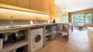 Une cuisine moderne avec des meubles en bois, un lave-linge encastré et une grande fenêtre qui laisse entrer la lumière naturelle.