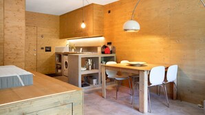 Une cuisine compacte avec des meubles en bois, un coin repas avec deux chaises et un lit placé dans un coin.