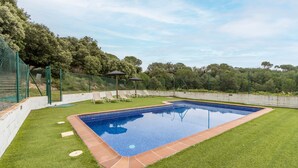 Piscina retangular com borda azulejada, rodeada por um gramado verde e um cercado.