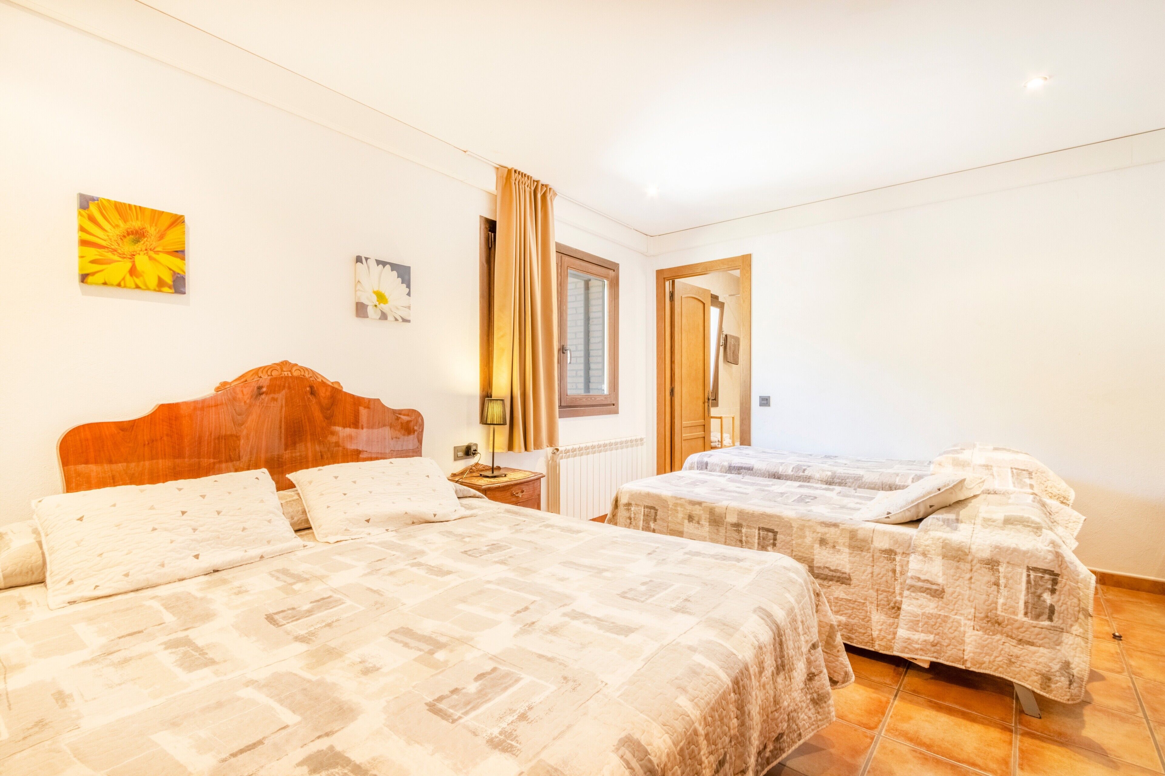 Une chambre avec deux lits, une tête de lit en bois, une fenêtre avec des rideaux et une porte.