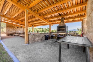 An outdoor patio with a stone wall, wooden beams, a metal table, and a brick oven.