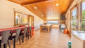 Een eetgedeelte met een lange tafel en stoelen, een keuken met inbouwapparatuur, en uitzicht op het omliggende landschap.
