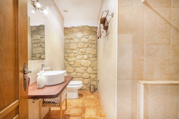 A bathroom with a stone wall, a sink, a toilet, and a shower area.