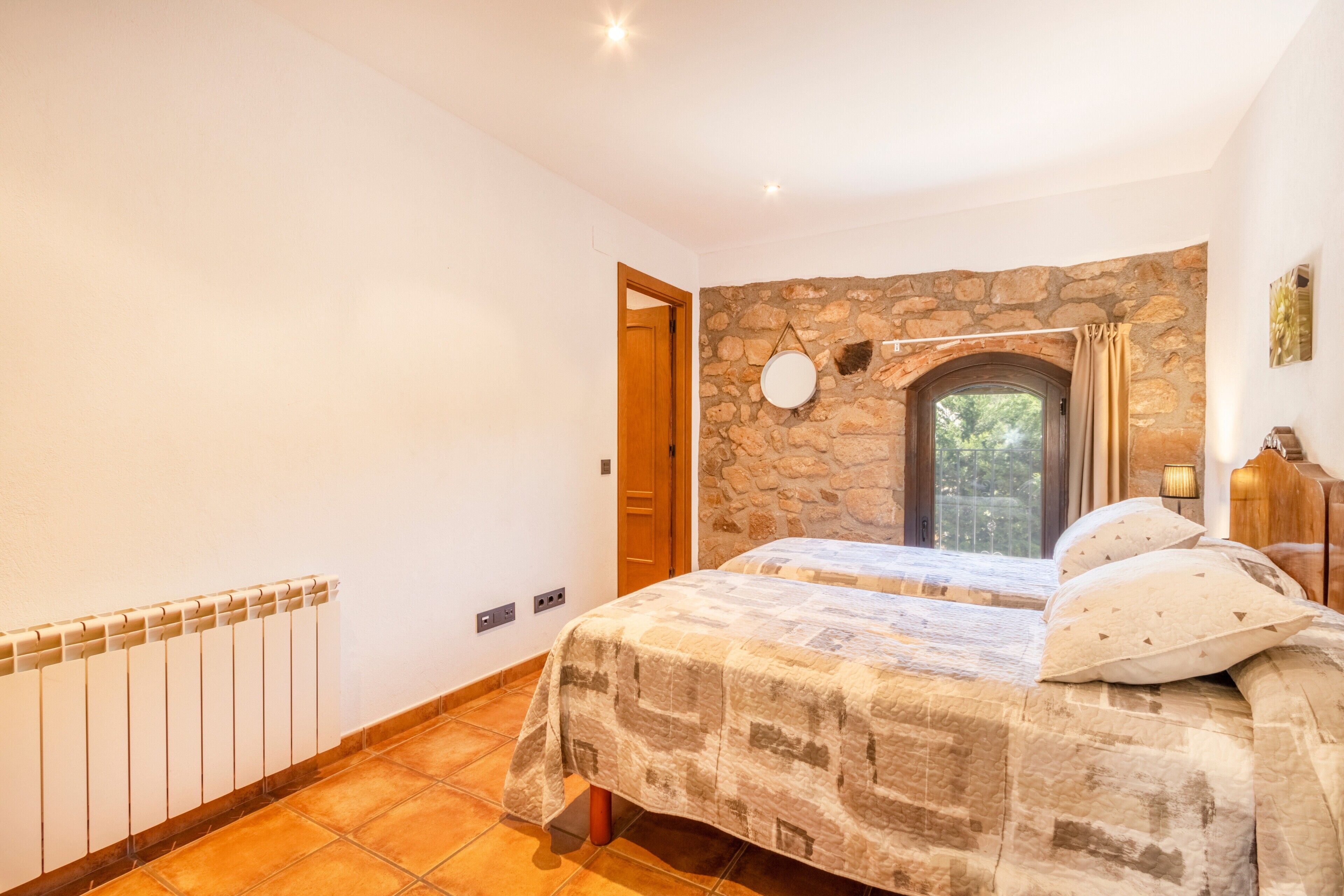Ein Schlafzimmer mit einer Steinstur, einem Bett mit gemustertem Überwurf, einem Heizkörper und einer Tür zu einem anderen Raum.