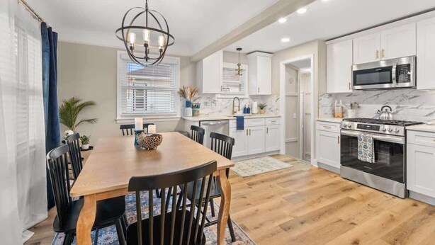 A modern kitchen with white cabinets, a wooden dining table, and a black chandelier. - Hot Tub - Shuffleboard - Sleeps 8 - Near Cleveland (Parma Heights)