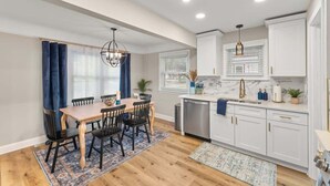 A modern kitchen with white cabinets, a wooden dining table, and a chandelier. - Hot Tub - Shuffleboard - Sleeps 8 - Near Cleveland (Parma Heights)