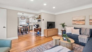 A modern living room with a sofa, coffee table, and TV. There is a dining area with chairs and a table in the background. - Hot Tub - Shuffleboard - Sleeps 8 - Near Cleveland (Parma Heights)