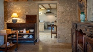 Une cuisine rustique avec des murs en pierre, des poutres en bois, un poêle et un coin repas comprenant une table et des chaises.