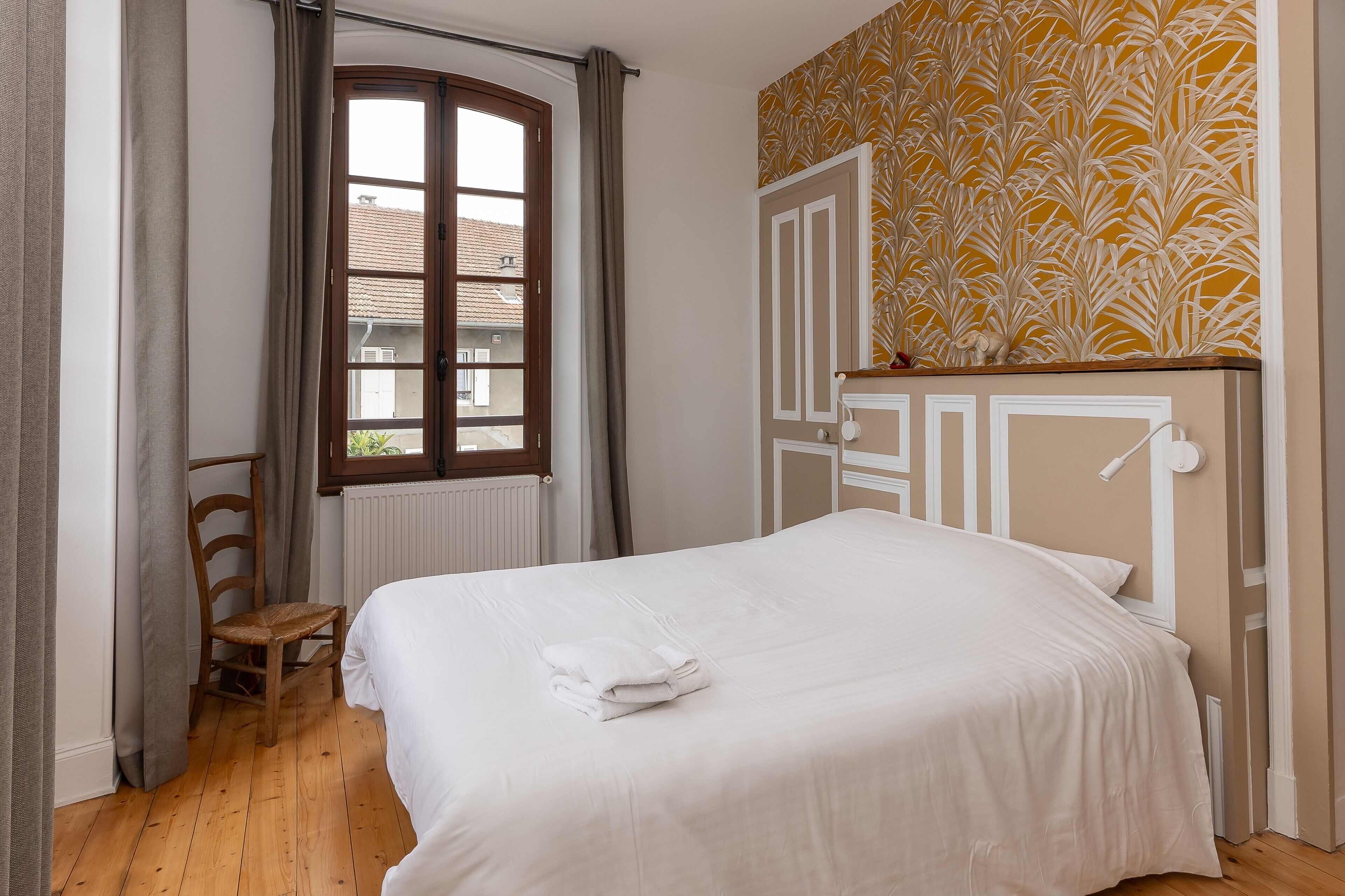 Une chambre à coucher avec un lit, une chaise, une fenêtre et un mur décoré de motifs.
