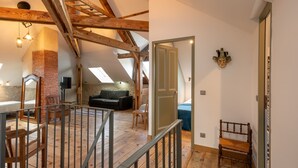 Une pièce de style « loft », avec des poutres en bois apparentes, une cheminée en briques, un canapé et une chaise en bois.