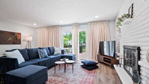 Ein modernes Wohnzimmer mit einem Ecksofa, einem Flachbildfernseher, einem Kamin und einem großen Fenster mit Vorhängen.