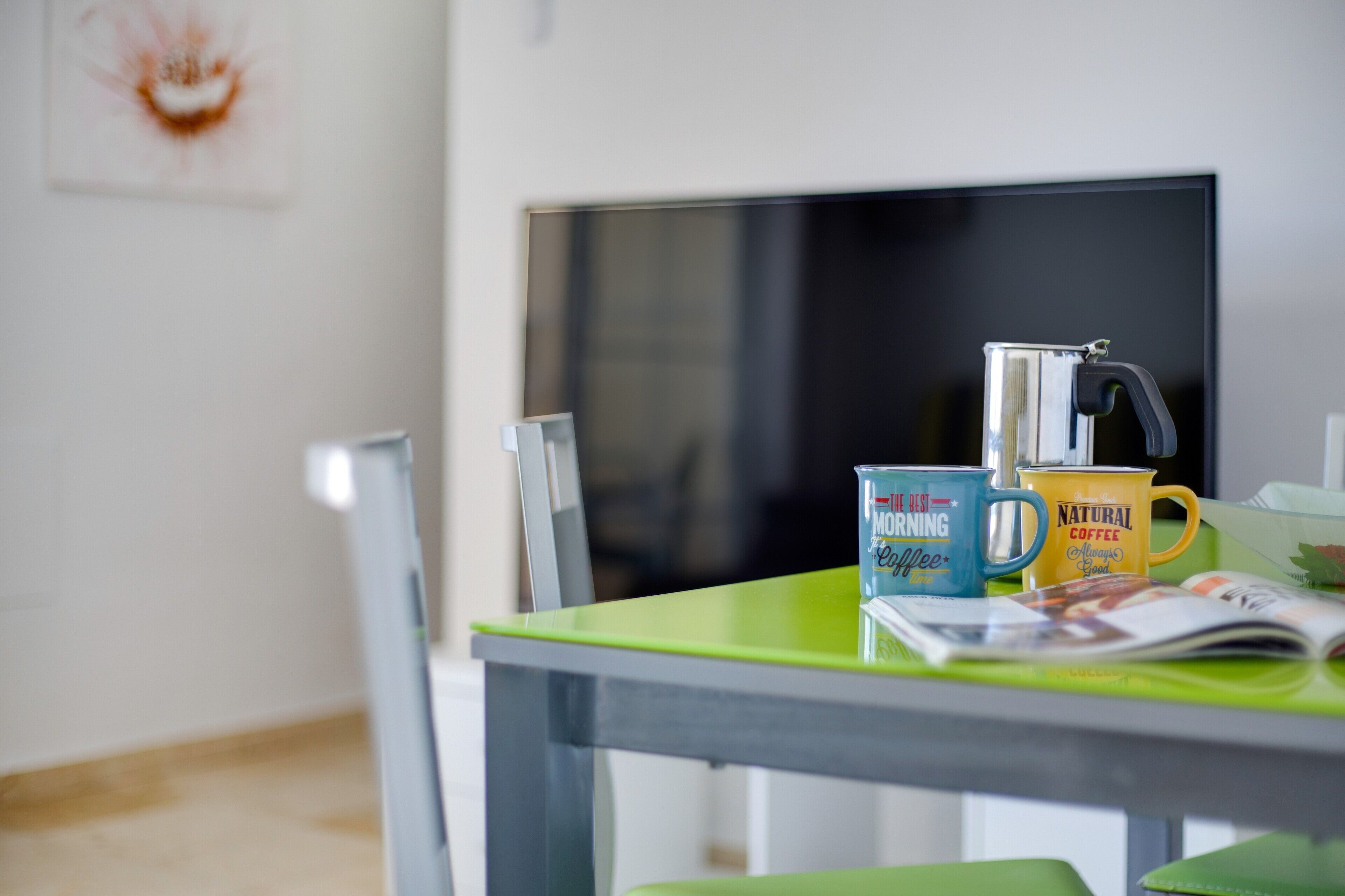 A room with a green table, a coffee maker, and two mugs with text.