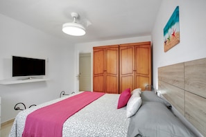 A bedroom with a bed, a TV, wooden wardrobe, and a painting on the wall.