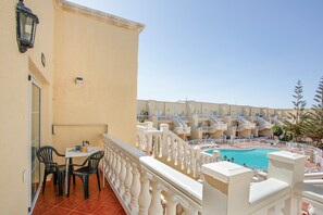 A balcony with a table and chairs, a pool, and a building with balconies. - Vacation Apartment 'Marysol' with Shared Pool, Private Terrace and Wi-Fi (Caleta de Fuste)